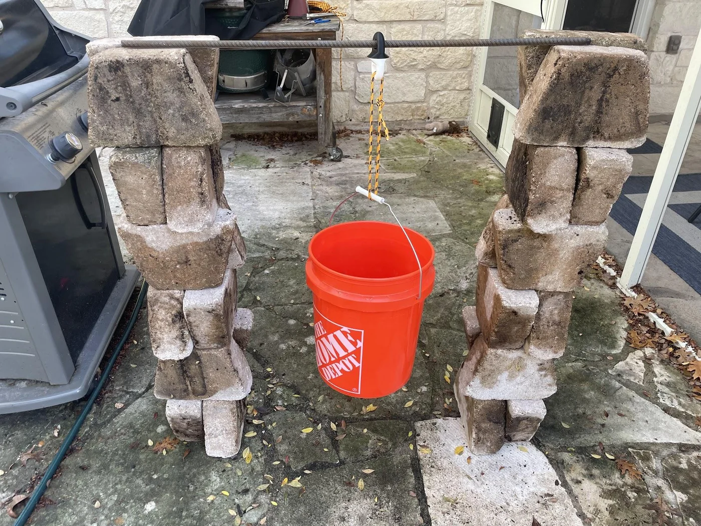 The test rig: a length of rebar resting on two stacks of bricks, with an orange bucket hanging from the test part on a rope.
